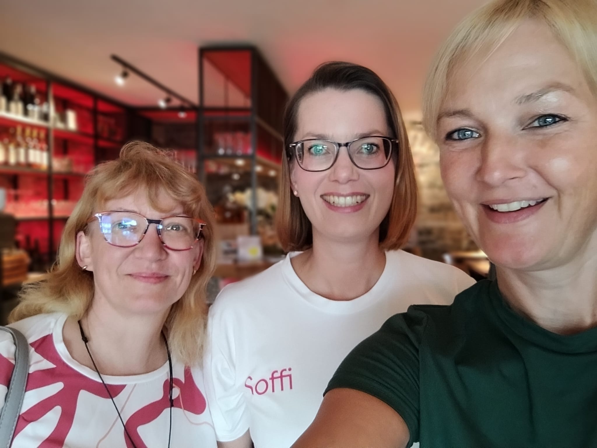 Drei lächelnde Frauen aus dem MindWeib-Netzwerk machen in einem Restaurant ein Selfie.