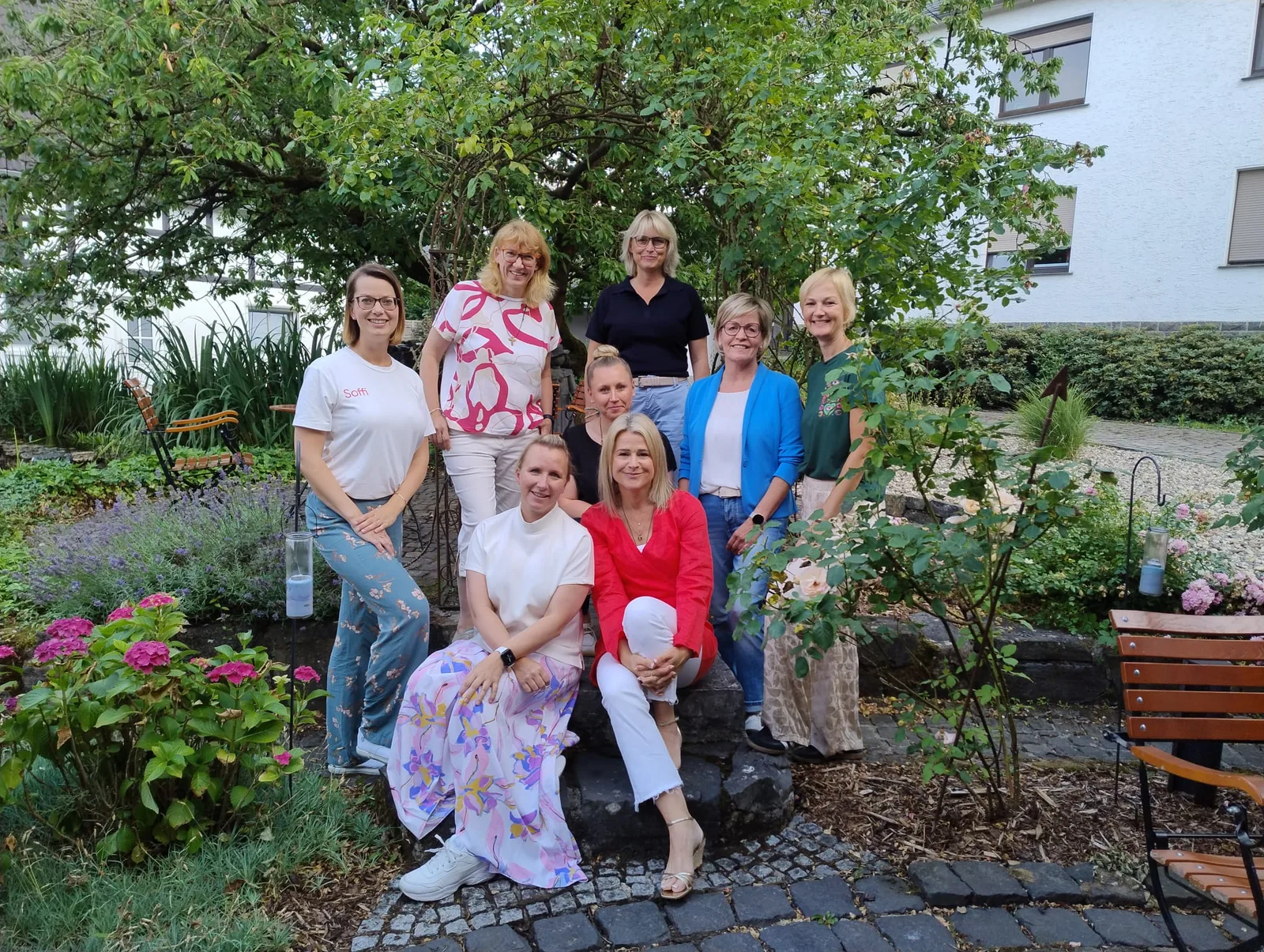 Acht Frauen aus dem MindWeib-Netzwerk stehen und sitzen für ein Gruppenfoto in einem blühenden Garten.